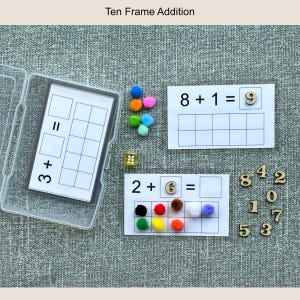May include: Educational ten frame addition set. Includes cards with addition problems, colorful pom-poms, wooden numbers, and a clear plastic case. The text "Ten Frame Addition" is at the top.