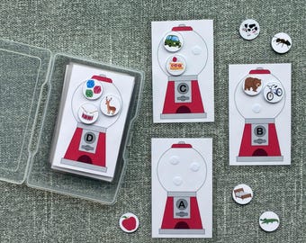 May include: A set of alphabet flashcards featuring gumball machine designs. Each card displays a letter and corresponding images. The cards are red and white, with a clear plastic case. The text "Digital Download - Gumball Alphabet Letters A-M" is at the top.