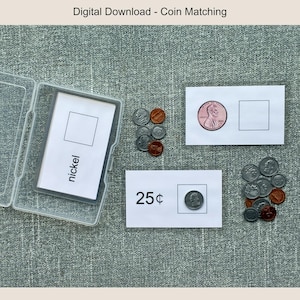 Op de afbeelding: Een munten-matching game met een doorzichtige plastic doos met kaarten met het label "nickel". Twee witte kaarten tonen een penny en een kwart dollar met een leeg vierkant. Losse munten liggen verspreid rond de kaarten.