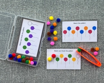 May include: Educational game with colorful pom-poms, cards, and an orange tweezer. The cards feature balloon patterns with the text "Match and finish the pattern" and "Match the pattern". A clear plastic case holds some of the pom-poms and cards.