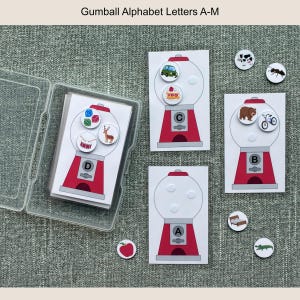 May include: Gumball alphabet flashcards A-M, featuring red and white gumball machine designs. Each card has a letter and corresponding images. Includes a clear plastic case for storage. Additional small circular images are also included.