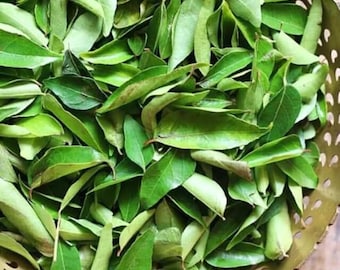 May include: A collection of fresh, vibrant green curry leaves piled inside a round, metallic gold-toned bowl featuring a decorative perforated pattern along its rim. The leaves are oval-shaped, pointed, and display various shades of green.