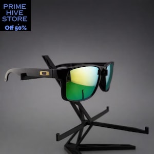 Peut inclure: Des lunettes de soleil noires avec des verres miroit&eacute;s verts sont pr&eacute;sent&eacute;es sur un pr&eacute;sentoir noir. Les lunettes ont une monture rectangulaire avec un accent dor&eacute; sur la branche. Les verres refl&egrave;tent une teinte jaune et verte. Le texte "PRIME HIVE STORE" et "Off 50%" est en haut &agrave; gauche.