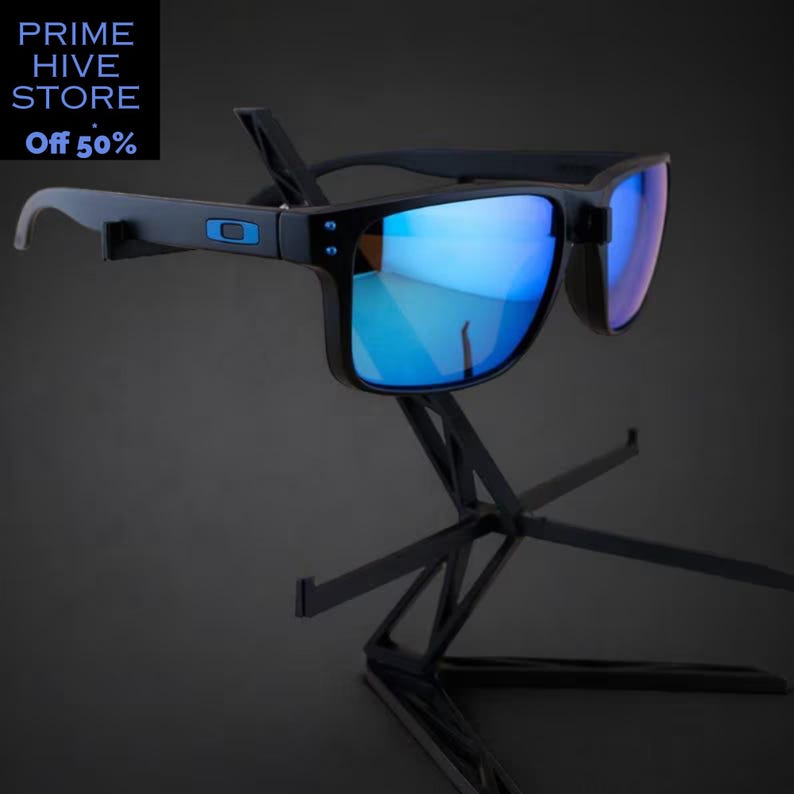 Peut inclure: Des lunettes de soleil noires avec des verres bleus miroir sont pr&eacute;sent&eacute;es sur un pr&eacute;sentoir noir. Les lunettes ont une monture rectangulaire et un petit logo bleu sur le c&ocirc;t&eacute;. Le texte "PRIME HIVE STORE" et "OFF 50%" est dans le coin sup&eacute;rieur gauche.