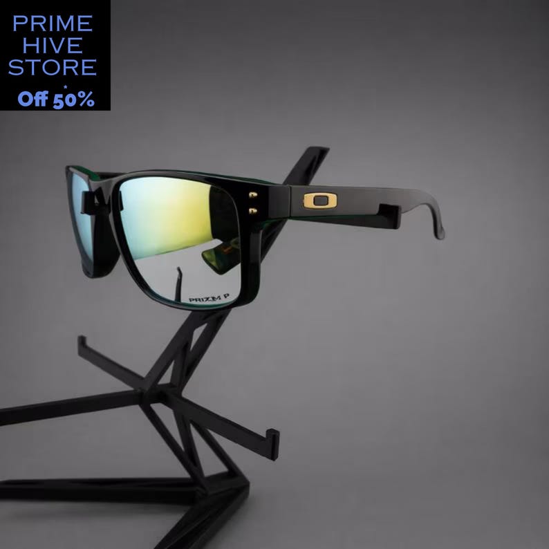 Peut inclure: Lunettes de soleil noires avec verres miroit&eacute;s, pr&eacute;sent&eacute;es sur un pr&eacute;sentoir noir. Les lunettes ont une monture rectangulaire avec un logo dor&eacute; sur la branche. Le texte "PRIZM P" est visible sur le verre. Le texte "PRIME HIVE STORE Off 50%" est &eacute;galement visible.