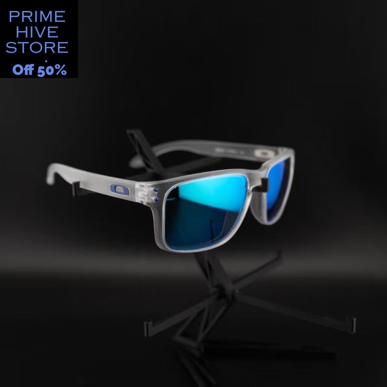 Peut inclure: Lunettes de soleil &agrave; monture transparente avec verres bleus miroir. Les lunettes de soleil sont pr&eacute;sent&eacute;es sur un support noir sur fond sombre. Le texte "PRIME HIVE STORE" et "Off 50%" est dans le coin sup&eacute;rieur gauche.