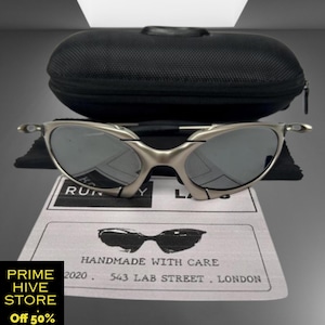 May include: Silver-framed sunglasses with dark lenses, resting on a white card with the text "HANDMADE WITH CARE" and the address "543 LAB STREET. LONDON." A black case sits behind the glasses. The text "PRIME HIVE STORE Off 50%" is in the lower left corner.