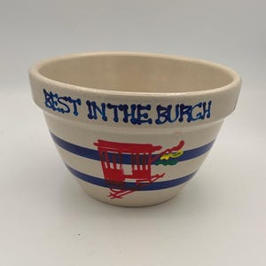 Könnte beinhalten: Cremefarbene Keramikschüssel mit blauen Streifen und dem Text "BEST IN THE BURGH" in Blau. Die Schüssel zeigt eine rot-gelbe Illustration einer Pferdekutsche. Ein dekorativer Küchenartikel.