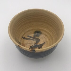 May include: A handmade ceramic bowl with a beige interior and a dark blue exterior. The bowl features a textured surface and a dark brown abstract design on the inside. The bowl is suitable for serving food.