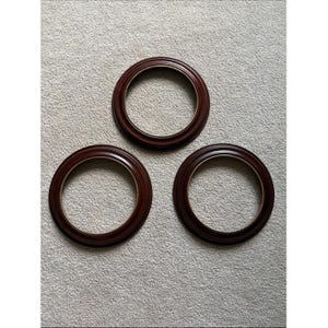 May include: Three circular picture frames with a dark mahogany wood finish. Each frame features a smooth, rounded profile with a thin, light-colored inner rim detail. The frames are empty, showing a hollow center within the circular structure.