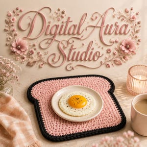 May include: A pink, bread-shaped crocheted trivet with a black border supports a plate with a fried egg. The image includes the text "Digital Aura Studio" with floral decorations, a candle, and a coffee cup, creating a breakfast setting.