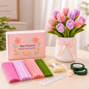 May include: A craft kit featuring a pink box labeled Pipe Cleaners Unleash Your Creativity, a white ribbed vase with a pink ribbon containing pink and purple pipe cleaner tulips, bundles of pink, purple, and green pipe cleaners, tape, and glue sticks.