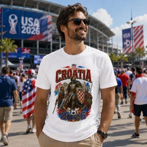 May include: White t-shirt featuring a graphic of a Croatian knight with a shield and the word "CROATIA" in red and blue. The shirt also includes the text "USA 2026" and a soccer ball design.