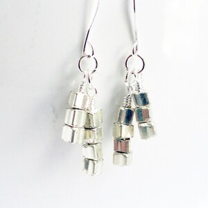 May include: Silver dangle earrings with multiple small silver beads hanging from the bottom of each earring.