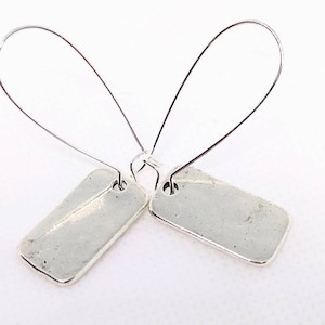 May include: A pair of silver earrings with rectangular charms hanging from thin silver hoops.