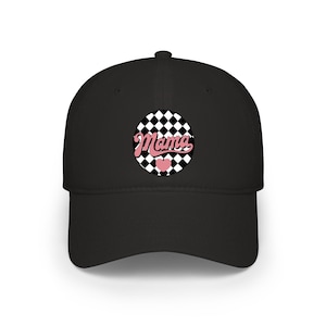 May include: Black baseball cap with a curved peak. The cap has a circular design with the word "Mama" in pink script, set against a black and white checkered background, and a pink heart.