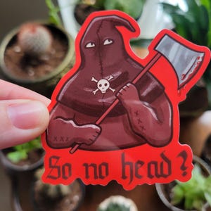 May include: A sticker depicting a cartoon executioner in a brown hood, holding a bloodied axe. A skull and crossbones are on the chest. The text "So no head?" is written in a gothic font at the bottom, on a red background.