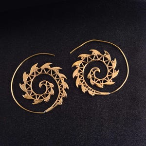 Può includere: Un paio di orecchini a cerchio color oro con un design a spirale, intricati motivi triangolari ritagliati e bordi appuntiti a forma di foglia che si estendono dalla bobina centrale. Struttura in filo metallico circolare sottile.