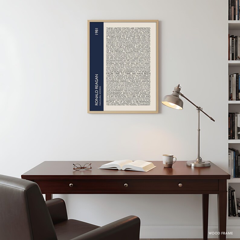K&ouml;nnte beinhalten: Ein gerahmter Druck mit Text aus Ronald Reagans Antrittsrede von 1981. Der Druck hat einen beigefarbenen Hintergrund mit schwarzem Text und einen vertikalen marineblauen Streifen mit dem Text "RONALD REAGAN INAUGURAL ADDRESS 1981". Der Rahmen ist aus Holz.
