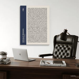 K&ouml;nnte beinhalten: Leinwanddruck mit dem Text von Ronald Reagans Antrittsrede von 1981. Der Druck hat einen cremefarbenen Hintergrund mit schwarzem Text und einen marineblauen vertikalen Streifen auf der linken Seite mit Name und Jahr.