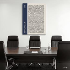 K&ouml;nnte beinhalten: Leinwanddruck mit Text aus Ronald Reagans Antrittsrede von 1981. Das Kunstwerk hat einen cremefarbenen Hintergrund mit schwarzem Text. Ein vertikaler marineblauer Streifen auf der linken Seite zeigt das Jahr und den Namen des Pr&auml;sidenten.