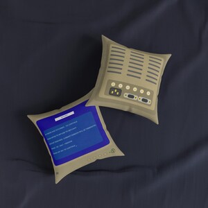 May include: Two square throw pillows featuring a beige computer monitor design. One pillow displays a blue screen with white text reading AN ERROR HAS OCCURRED, while the other shows the beige back panel with ventilation slots and ports.