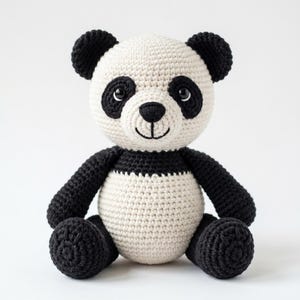 May include: A handmade crochet panda bear with a cream-colored body, black arms, legs, and ears. The panda has black eye patches, a black nose, and a smiling mouth. The stuffed animal is sitting upright, with its arms and legs extended.