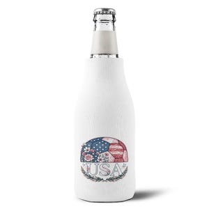 Puede incluir: Una funda enfriadora blanca para botella con un gráfico de un balón de fútbol con estrellas y rayas rojas, blancas y azules, decorado con flores. Debajo del balón, el texto USA aparece en una fuente serif, enmarcado por hojas verdes.