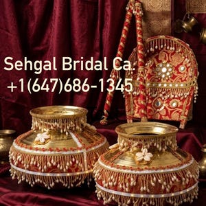 May include: Two brass pots decorated with red fabric, white trim, and hanging shell tassels. Behind them is a red fabric fan with mirrors and two matching sticks. Text reads: Sehgal Bridal Ca. +1(647)686-1345. The items feature intricate gold-toned metalwork.
