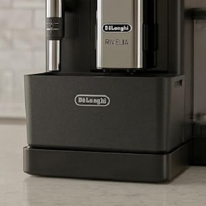 May include: A black De'Longhi Rivelia coffee machine with a silver front panel, a clear bean hopper filled with dark coffee beans, a side water reservoir, and a milk frothing wand. The brand name De'Longhi is printed on the front and the drip tray.