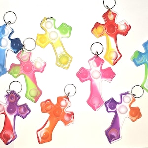 May include: A collection of twelve cross-shaped keychains made of silicone, each featuring integrated circular push-pop bubbles. The keychains display various multi-colored swirl patterns, including combinations of pink, blue, yellow, green, orange, and purple, all attached to silver-toned metal key rings.