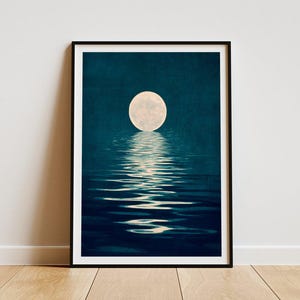 Pode incluir: Impressão artística emoldurada que retrata uma lua cheia refletida em água ondulada. A obra apresenta um fundo azul escuro com uma lua brilhante e circular e seu reflexo brilhante. A impressão está emoldurada em preto.