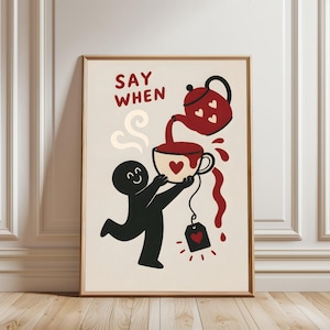 May include: A framed wall art print on a cream background featuring a black cartoon figure holding a white teacup with a red heart. A red teapot with white hearts pours liquid into the cup, with the text SAY WHEN in red above the teapot.