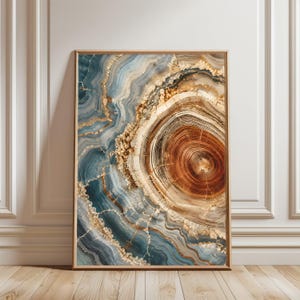 Puede incluir: Impresión artística abstracta que presenta una vista detallada y de cerca de una sección transversal de un tronco de árbol. La obra de arte muestra anillos concéntricos en tonos de marrón, beige y dorado, con vetas azules y doradas. La impresión está enmarcada en un marco de madera marrón claro.