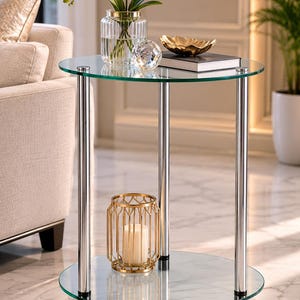May include: A round side table featuring two clear glass tiers supported by three polished chrome metal legs. The table has a transparent circular top and a matching circular bottom shelf, providing a sleek structure for displaying decorative items.