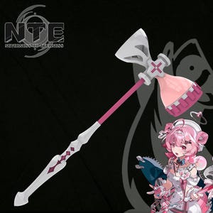 Puede incluir: Un arma de utilería de mango largo con un eje rosa y una cabeza de martillo blanca y rosa con un símbolo de cruz. El diseño incluye un mango blanco con recortes en forma de diamante y una ilustración de personaje con pelo rosa y traje blanco.