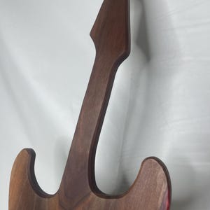 May include: A wooden guitar-shaped object with a dark brown finish. The instrument's body and neck are visible, showcasing the wood grain. The edges of the guitar have a red accent. The design is a stylized representation of a guitar.