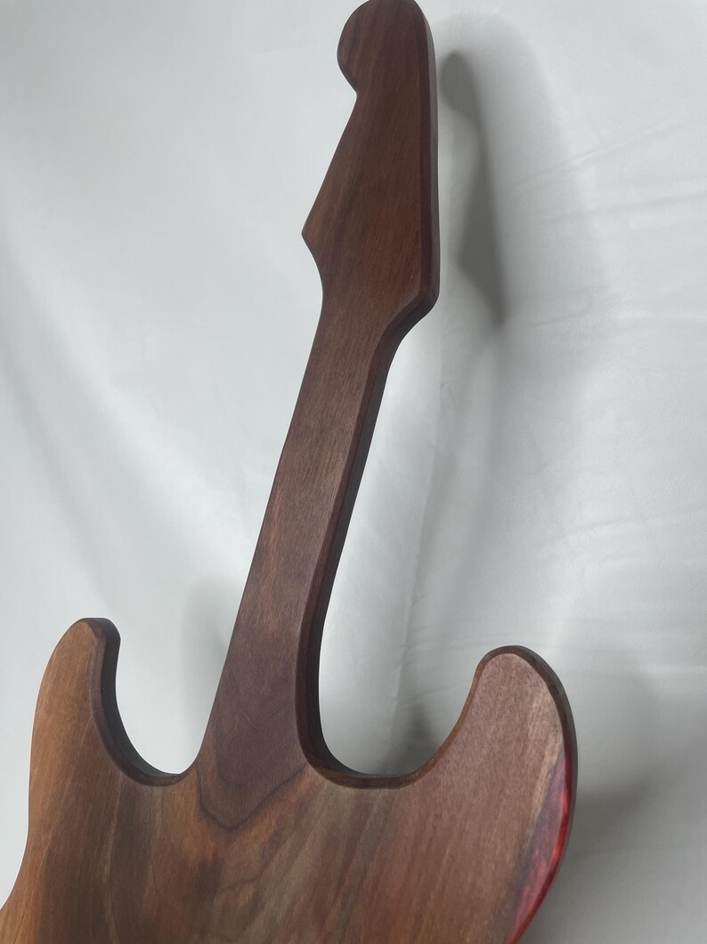 May include: A wooden guitar-shaped object with a dark brown finish. The instrument's body and neck are visible, showcasing the wood grain. The edges of the guitar have a red accent. The design is a stylized representation of a guitar.