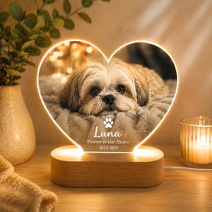 May include: A heart-shaped LED lamp featuring a photograph of a light-colored Shih Tzu dog. The lamp base is light wood. Text on the lamp reads: Luna, a paw print icon, Forever in Our Hearts, and the years 2013-2024 in white lettering.