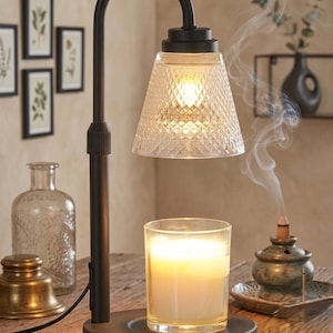 May include: A black metal candle warmer lamp with an adjustable height arm and a clear, diamond-patterned glass shade. The lamp features a circular base that holds a glass jar candle, which is illuminated by the heat source from the lamp above.