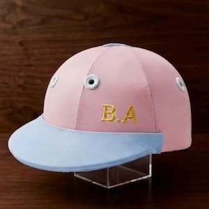 Puede incluir: Una gorra de béisbol rosa claro con visera azul claro y ojales blancos. El panel frontal presenta las letras doradas bordadas B.A. La gorra está confeccionada con seis paneles y tiene una corona estructurada de diseño bicolor.