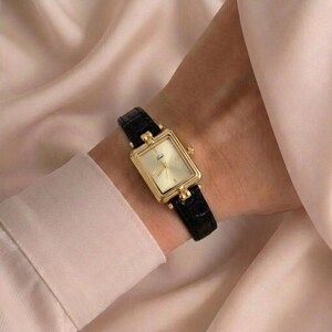 Women's quartz wristwatch with rectangular gold case and black leather band.