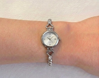 Montre-bracelet à quartz pour femme avec boîtier rond en argent, cadran blanc et bracelet en forme de cœur.