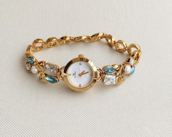 Women's quartz wristwatch with round gold case, white dial and pearl crystal charm bracelet