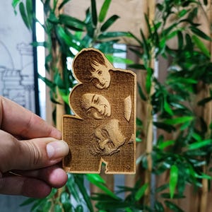 May include: A wooden plaque featuring a carved image of two people embracing. The plaque is rectangular with a unique cutout design. The wood has a warm, natural tone, and the carving details are visible. The background includes bamboo stalks and green leaves.