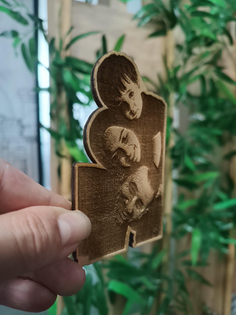May include: A wooden cutout featuring three engraved faces. The faces are of different sizes and appear to be portraits. The wood has a warm, brown tone, and the details of the faces are visible.