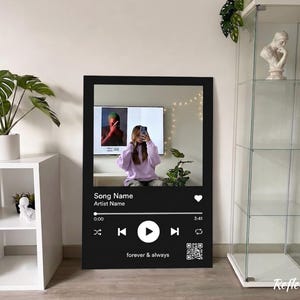 May include: A rectangular black mirror featuring a white graphic overlay that mimics a music streaming interface. The design includes a central square frame for reflection, song and artist name placeholders, a progress bar, playback controls, a heart icon, and a QR code with the text "forever & always" at the bottom.