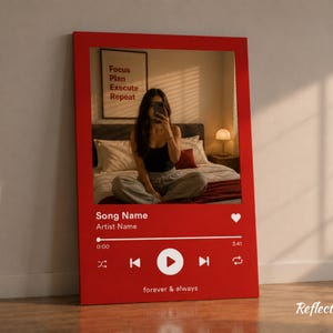 Puede incluir: Impresión en lienzo enmarcada en rojo con un diseño de interfaz de reproductor de música. La impresión incluye el texto "Song Name", "Artist Name" y "forever & always". El fondo muestra a una persona tomando una foto en un dormitorio.
