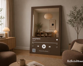 以下が含まれることがあります： 音楽プレーヤーのインターフェースデザインが施された、大きくて長方形の茶色の鏡。 鏡はニュートラルな色調の部屋、丸い照明器具、小さな木を映し出しています。 「Song Name」、「Artist」、「forever & always」の文字が見えます。