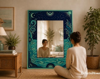 以下が含まれることがあります： 天体と水生のデザインが施された装飾フレーム付きの大きな長方形の鏡。 フレームはティールとネイビーブルーで、月、太陽、星、波、アヒルのイラストが描かれています。 鏡は床に座っている女性を映しています。
